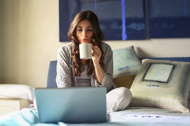 Žena sediaca na posteli s notebookom, ktorá pije kávu.jpg